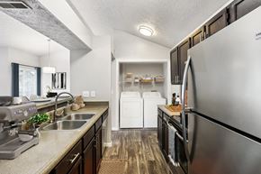Cincinnati apartment for rent - A modern kitchen with a stainless steel refrigerator, a washer and dryer stacked in the corner, and a dining area with a table and chairs.