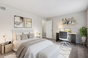 Cincinnati apartment for rent - A bedroom with a large bed, a desk with a chair, and a potted plant.