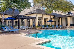 Frisco apartment for rent - A pool area with a building in the background and lounge chairs and umbrellas.