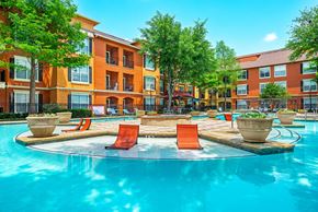 Irving apartment for rent - A swimming pool surrounded by orange chairs and potted plants in front of a multi-story apartment building.