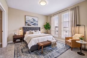 Denver apartment for rent - A bedroom with a large bed, a bench, a chair, and a plant.