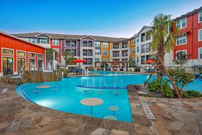 San Antonio apartment for rent - A pool surrounded by a stone patio and a building with red and orange walls.