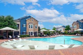 Prosper apartment for rent - A swimming pool surrounded by lounge chairs and umbrellas in front of a building.