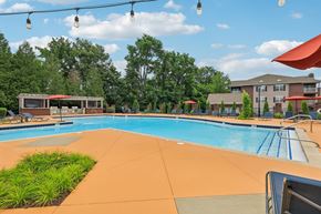 Murfreesboro apartment for rent - A large outdoor swimming pool with a red umbrella and a building in the background.