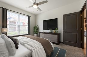 Louisville apartment for rent - A bedroom with a bed, a ceiling fan, a television, and a window with blinds.