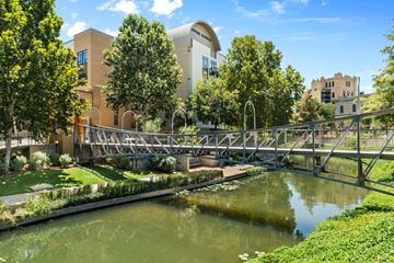 San Antonio apartment for rent - A bridge over a green waterway with trees and buildings in the background.