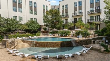 San Antonio apartment for rent - A swimming pool surrounded by chairs and umbrellas in front of apartment buildings.
