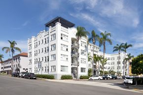 San Diego apartment for rent - A white building with a black roof and palm trees in front.