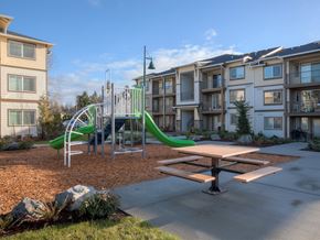 Mill Creek apartment for rent - A playground with a green slide and a picnic table in front of apartment buildings. at Mill Creek Meadows Apartments, Mill Creek