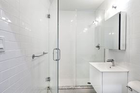 Brooklyn apartment for rent - A white tiled bathroom with a walk-in shower and a white sink vanity.