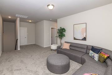 Waxahachie apartment for rent - A living room with a grey couch and a round ottoman.