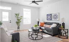 St. Peters apartment for rent - A living room with a grey couch, a black and white patterned rug, and a ceiling fan.