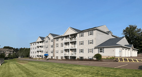 Moncton apartment for rent - A large building with a grey roof and white walls with balconies on the second floor.