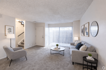 Las Vegas apartment for rent - A living room with a grey couch, a grey armchair, a black side table, and a coffee table with a plant on it.
