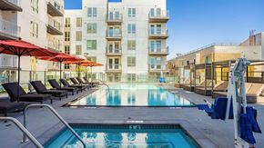 Los Angeles apartment for rent - A swimming pool surrounded by lounge chairs and umbrellas in front of apartment buildings.