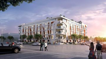 Los Angeles apartment for rent - A modern building with a curved facade and a large glass window is surrounded by a parking lot with cars and pedestrians.