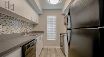 A kitchen with a black refrigerator, a sink, and a window with blinds.