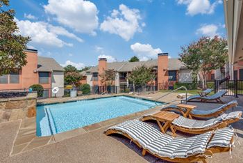 A pool surrounded by lounge chairs and a fence.