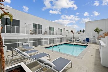 A pool area with sun loungers and a white building in the background.