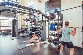 Tempe apartment for rent - A man is lifting a barbell in a gym with a woman stretching on the floor.