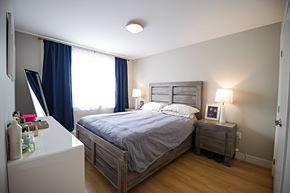 Halifax apartment for rent - A bedroom with a bed, nightstand, and window with blue curtains.