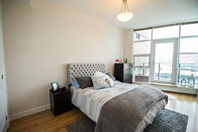 Halifax apartment for rent - A bedroom with a large bed and a window overlooking a cityscape.