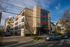 Halifax apartment for rent - A modern building with a brick facade and a glass entrance is surrounded by parked cars.