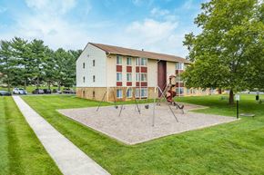 Hagerstown apartment for rent - A playground with swings and a slide is in front of a two-story apartment building.