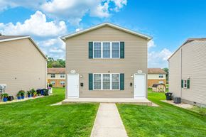 Hagerstown apartment for rent - A beige house with green shutters and a white door is in the foreground with a clear blue sky above.