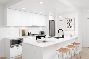 Vancouver apartment for rent - A kitchen with white cabinets and a white countertop with a sink and bar stools.