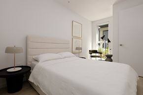 Vancouver apartment for rent - A white bed with a black table and a lamp on it.