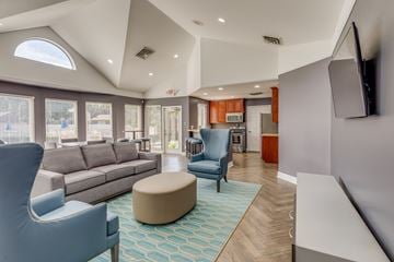 Livonia apartment for rent - A living room with a grey sofa, a blue armchair, a white chair and a TV mounted on the wall.