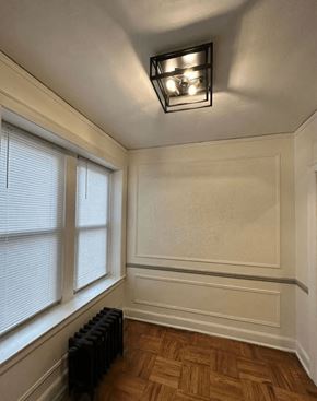 Detroit apartment for rent - A room with a wooden floor, a window with blinds, a radiator, and a light fixture.