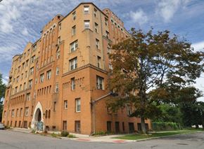 Detroit apartment for rent - A large red brick building with a tree in front.