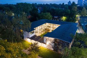 Detroit apartment for rent - A modern building with a dark roof and lit windows is surrounded by trees.