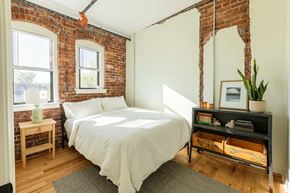 Detroit apartment for rent - A bedroom with a bed, nightstand, and a brick wall.