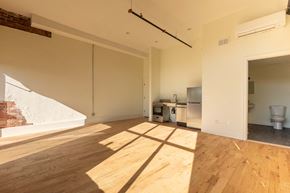 Detroit apartment for rent - A room with wooden floors and white walls, with a kitchen area visible in the background.