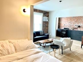 Detroit apartment for rent - A bedroom with a white bed and a black chair.