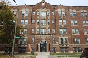 Detroit apartment for rent - A large red brick building with a black car parked in front.
