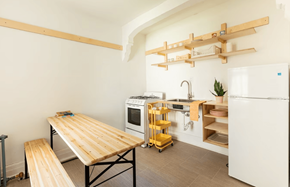 Detroit apartment for rent - A kitchen with a white refrigerator, a wooden table and bench, and a yellow rolling cart.