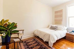 Detroit apartment for rent - A bedroom with a white bed and a plant on a side table.