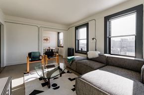 Detroit apartment for rent - A living room with a grey couch and a glass table.