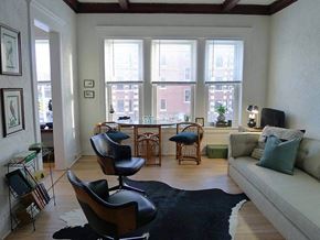 Detroit apartment for rent - A living room with a black and white cowhide rug, a black leather chair, a grey couch, and a wooden floor.
