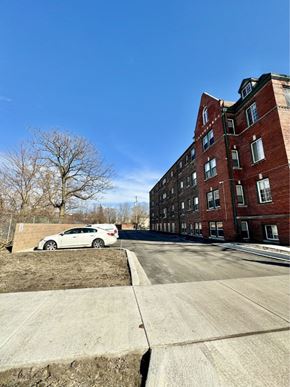 Detroit apartment for rent - A white car is parked on a concrete driveway in front of a red brick building.