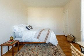 Detroit apartment for rent - A bedroom with a bed, a small table, a rug and a basket on the floor.