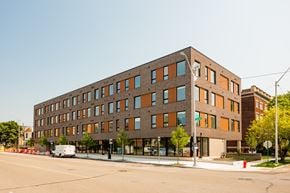 Detroit apartment for rent - A large building with a brown and orange facade sits on a street corner.