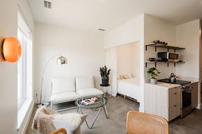 Detroit apartment for rent - A modern living room with a white couch, a glass coffee table, and a kitchen area in the background.