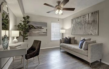Dallas apartment for rent - A living room with a grey couch, a chair, a table with a vase and a lamp on it, and a painting on the wall.