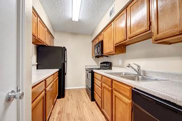 Red Oak apartment for rent - A kitchen with wooden cabinets and black appliances.