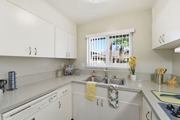 Sunnyvale apartment for rent - A kitchen with white cabinets and a window with a view of a balcony with a yellow towel hanging on the sink.